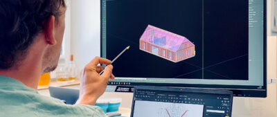 Mann mit Bleistift prüft AutoCAD 3-D-Modell eines Hauses am Bildschirm - LORENZ stellt alle seine Produkte mit den möglichen Bauweisen als digitale Bausteine zur verfügung