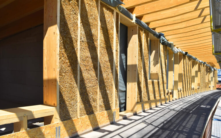 Fassadenansicht des Mehrgenerationen-Hybridbaus in Kassel mit goldglänzender Strohoberfläche mit LORENZ DD-Montagesystemen aus Holz und Stroh zum Dämmen und Bauen.